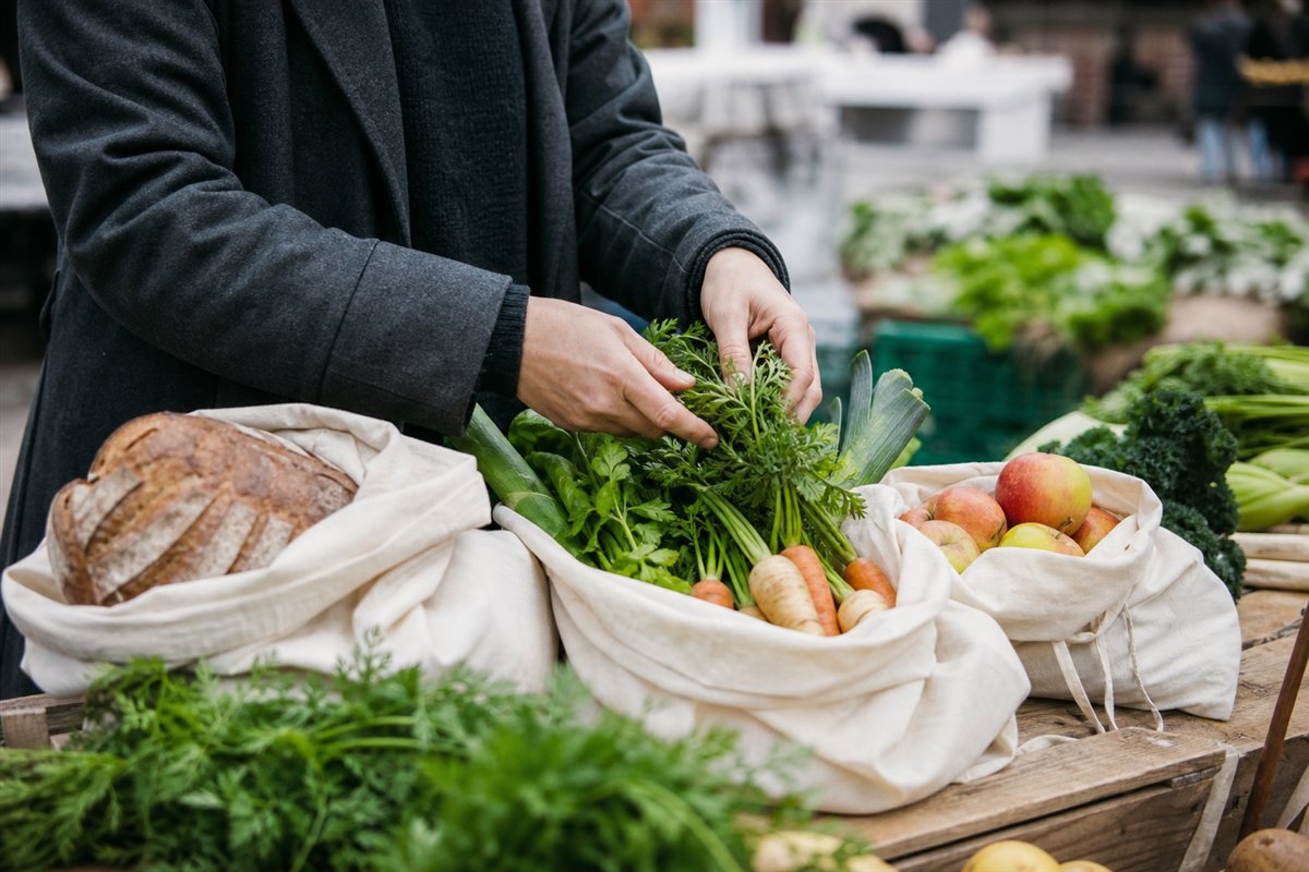 Stoffbeutel mit Brot, Äpfeln, Kräutern und Wurzelgemüse auf einem Marktstand